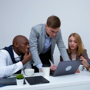 Three colleagues engaged in teamwork around a laptop in a modern office setting.